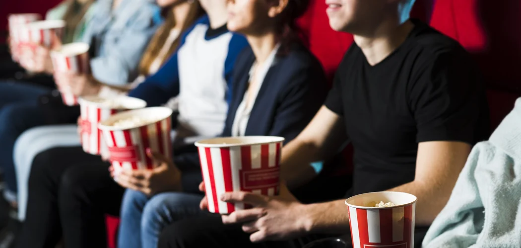 Pessoas assistindo a um filme no cinema com baldes de pipoca