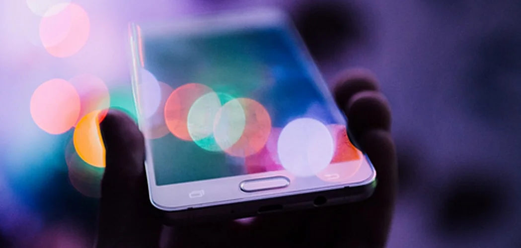 Mão segurando um smartphone com luzes coloridas na tela