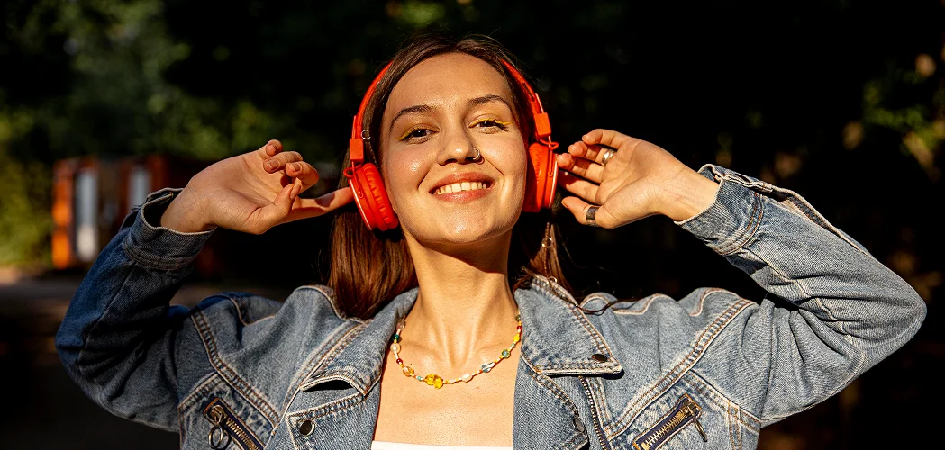 Mulher sorrindo ao ar livre com fones de ouvido vermelhos, ouvindo música