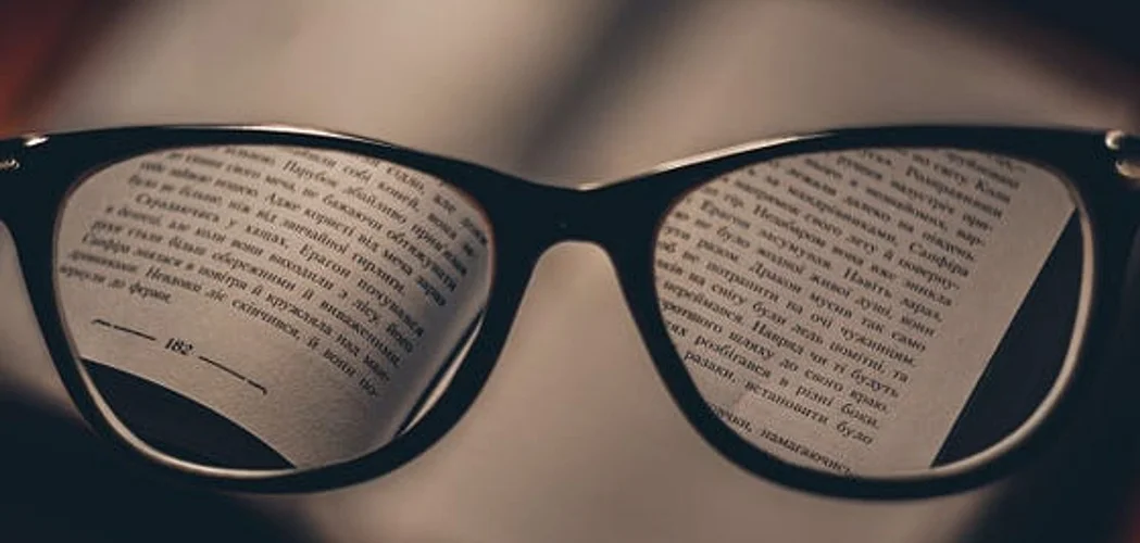 Óculos sobre um livro aberto com texto desfocado ao fundo